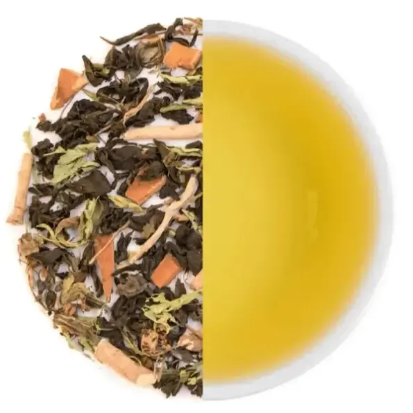 Loose tea leaves with chips of bark and root beside a white cup of pale golden tea, seen from above